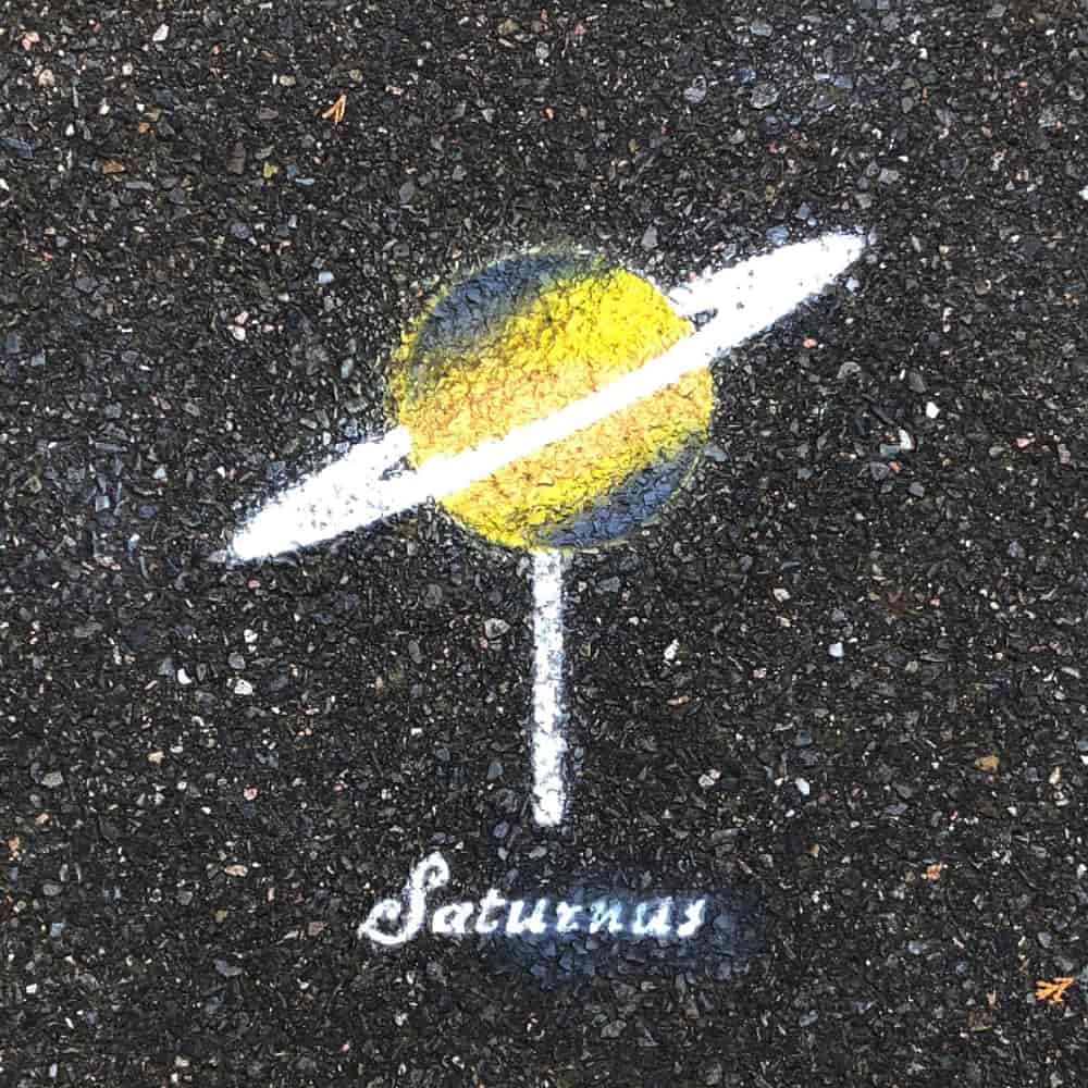 Planet Saturn, 12 cm in diameter, painted on the pavement with the Latin name tag Saturnus.